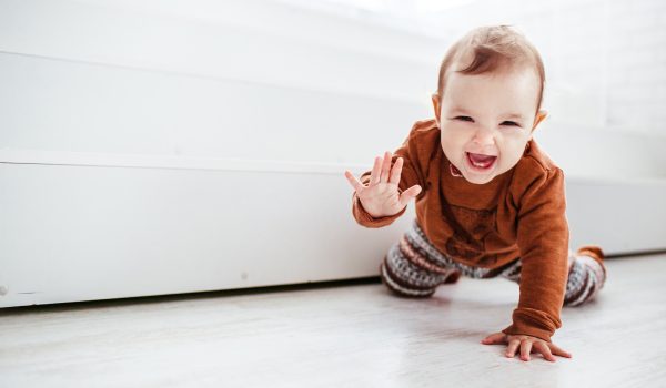 Happy child in orange sweater plays with feather on the floor