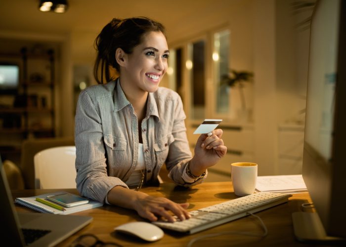 Mujer joven feliz usando tarjeta de crédito para comprar en línea por la noche en casa.